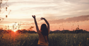 Woman standing in a field at sunset with arms raised, representing personal empowerment in taking charge of heart health